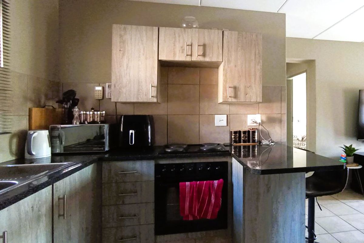 A functional kitchen featuring wood-look cabinetry, dark granite countertops, a built-in electric oven and hob, and a tiled backsplash.