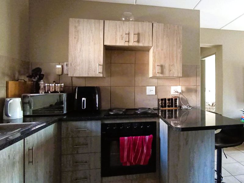 A functional kitchen featuring wood-look cabinetry, dark granite countertops, a built-in electric oven and hob, and a tiled backsplash.