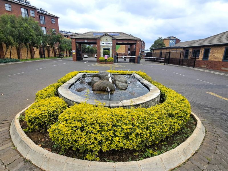 The entrance to the Oxford Heights complex features a secure gatehouse, paved driveway, and a central landscaped water feature.