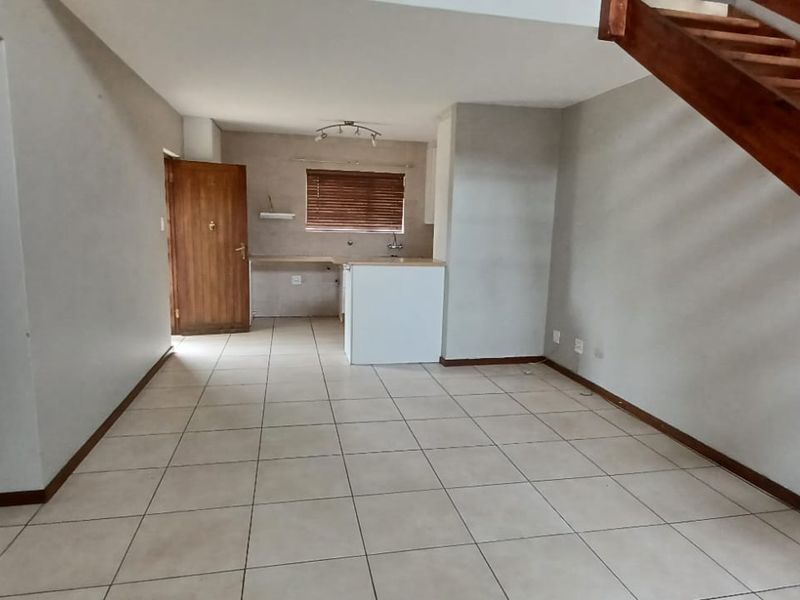 An open-plan living and kitchen area featuring tiled flooring and a wooden staircase leading to the upper level.