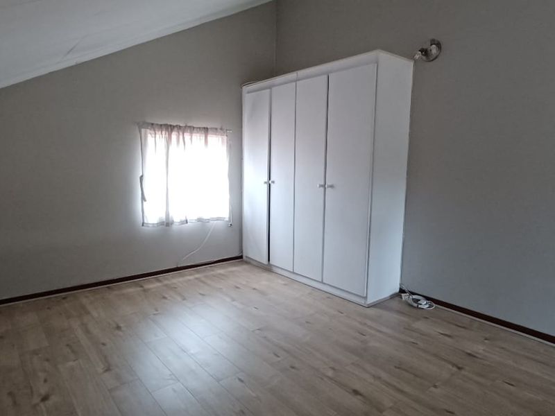 A bright, empty bedroom featuring laminate flooring, a sloped ceiling, and a built-in white wardrobe.
