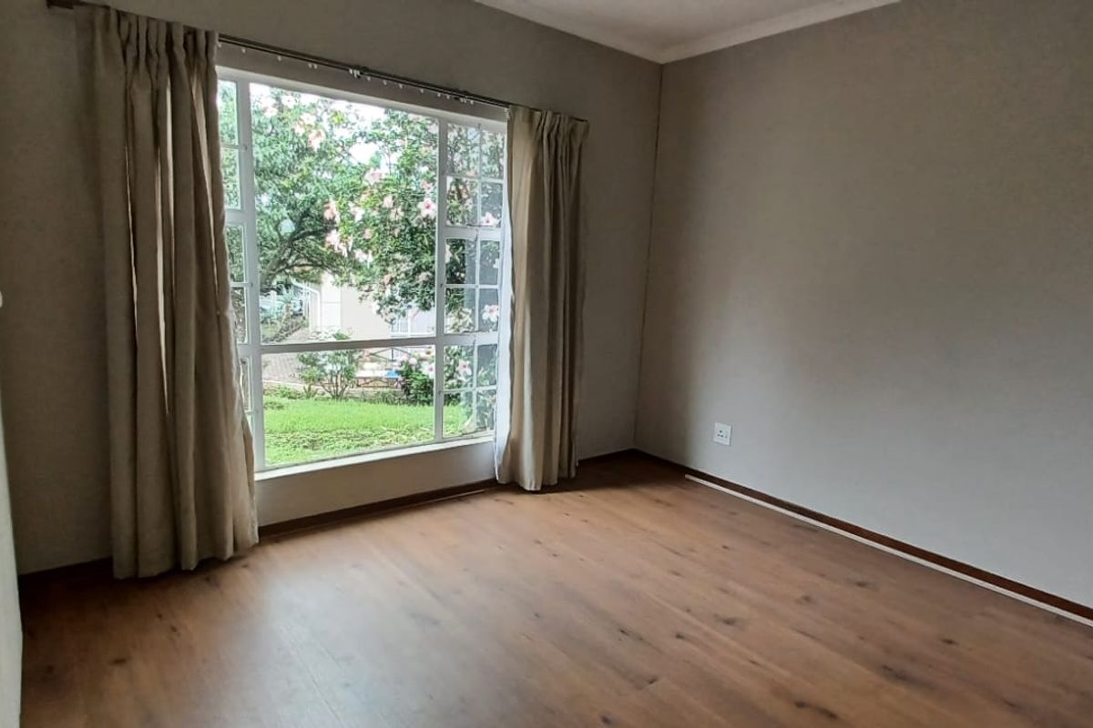 A bright, empty bedroom featuring laminate flooring, a built-in wardrobe, and a large window overlooking the garden.