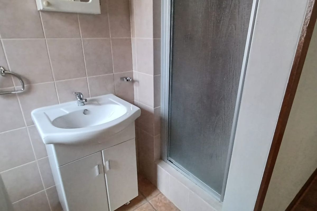 A compact bathroom featuring a vanity cabinet with a washbasin and a separate shower enclosure with tiled wall finishes.