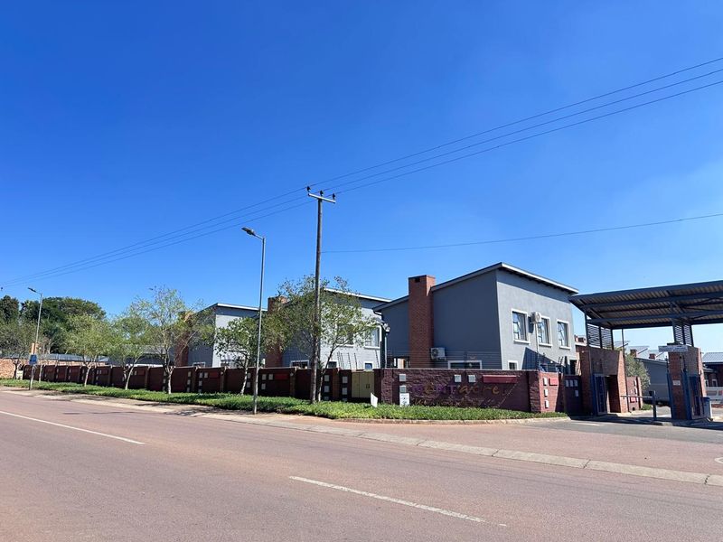 Street view of the townhouse complex entrance, featuring a secure perimeter brick wall with electric fencing and a gated access point.