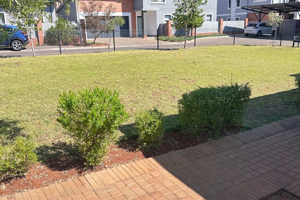 A view of a well-maintained rear garden featuring a paved walkway, manicured lawn, and perimeter fencing, overlooking neighboring townhouse properties.
