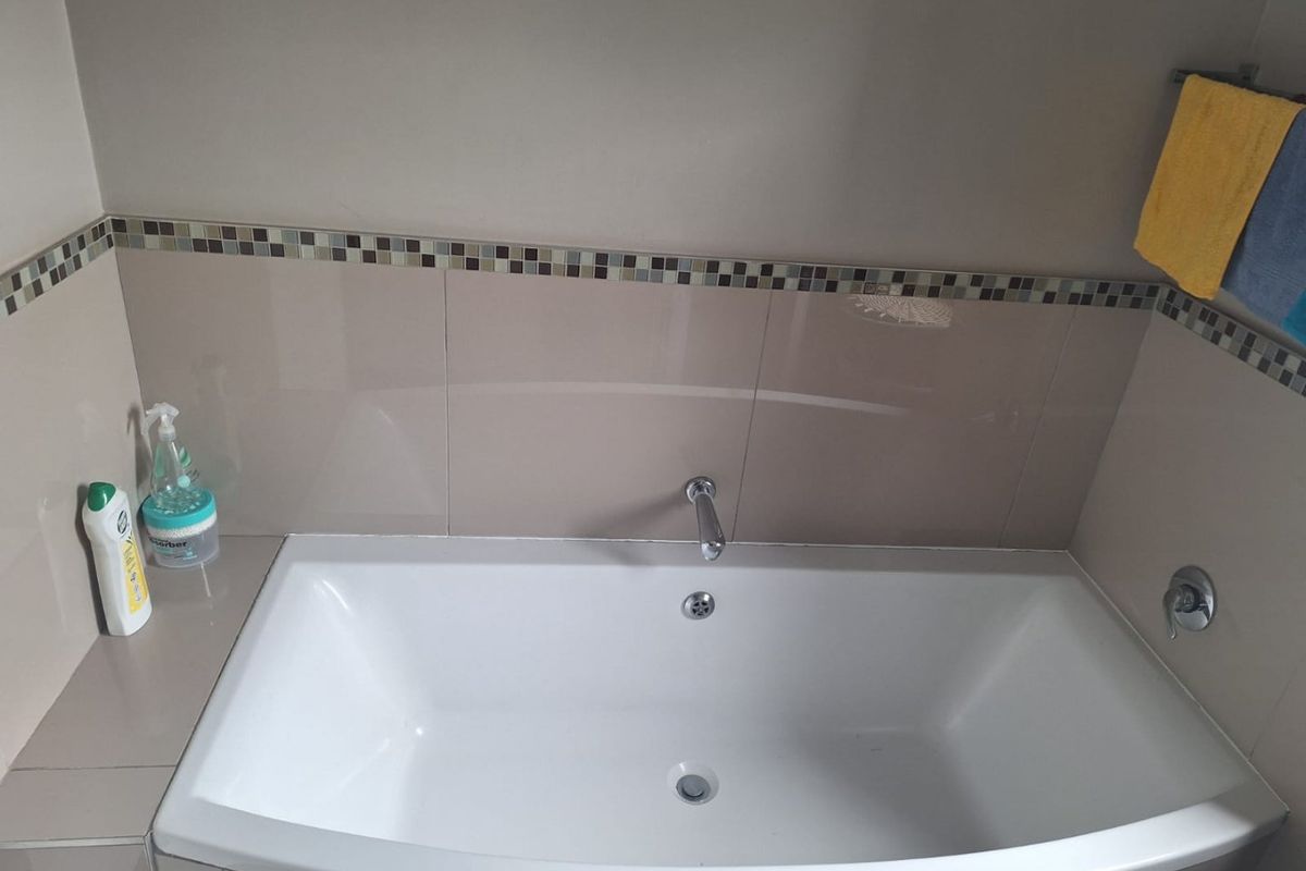 A clean bathroom featuring a built-in bathtub with wall-mounted fixtures and a decorative mosaic tile border.