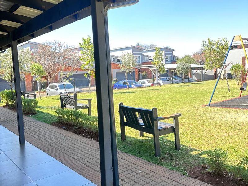 A covered patio area overlooking a communal garden with paved walkways and playground facilities within the townhouse complex.
