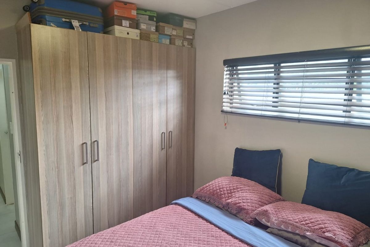 A functional bedroom featuring a large built-in wardrobe with wood-grain finish and horizontal venetian blinds for privacy.