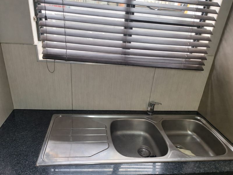 A clean kitchen sink area featuring a stainless steel double bowl sink, granite countertop, and modern wall paneling with fitted venetian blinds.