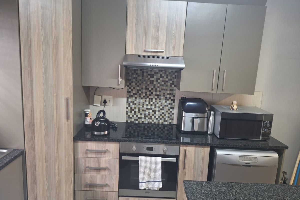 Modern kitchen featuring wood-grain and grey cabinetry, granite countertops, mosaic tile backsplash, and built-in appliances including an oven, hob, and extractor fan.