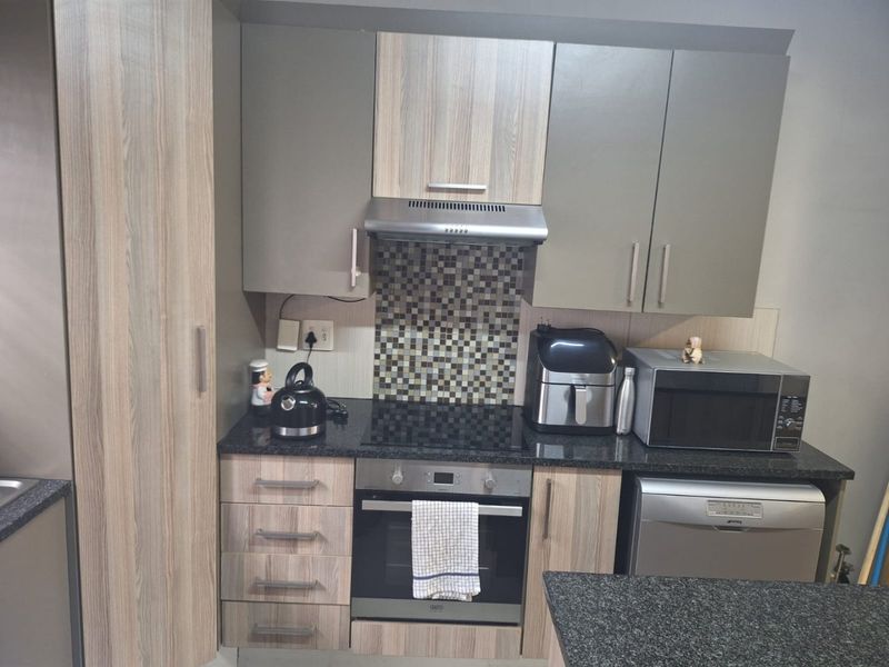 Modern kitchen featuring wood-grain and grey cabinetry, granite countertops, mosaic tile backsplash, and built-in appliances including an oven, hob, and extractor fan.
