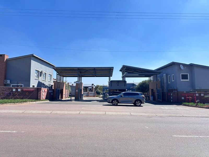 Front entrance view of the townhouse complex featuring a secure gated access point with modern architectural structures and perimeter fencing.