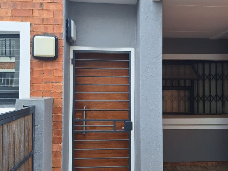 A secure townhouse entrance featuring a modern wood-look security gate, brick and rendered facade, and paved exterior walkway.