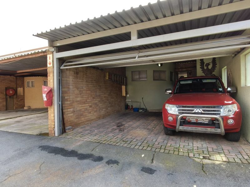 A functional double carport or garage area featuring brick walls, paved flooring, and a corrugated metal roof structure.