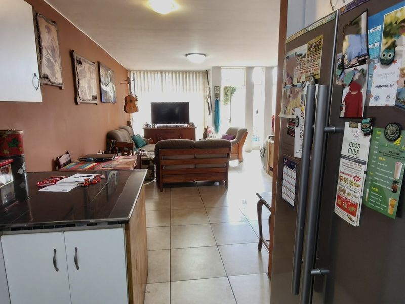 Open-plan living area featuring a kitchen with built-in cabinetry and tiled flooring, flowing into a lounge space with access to an outdoor area.