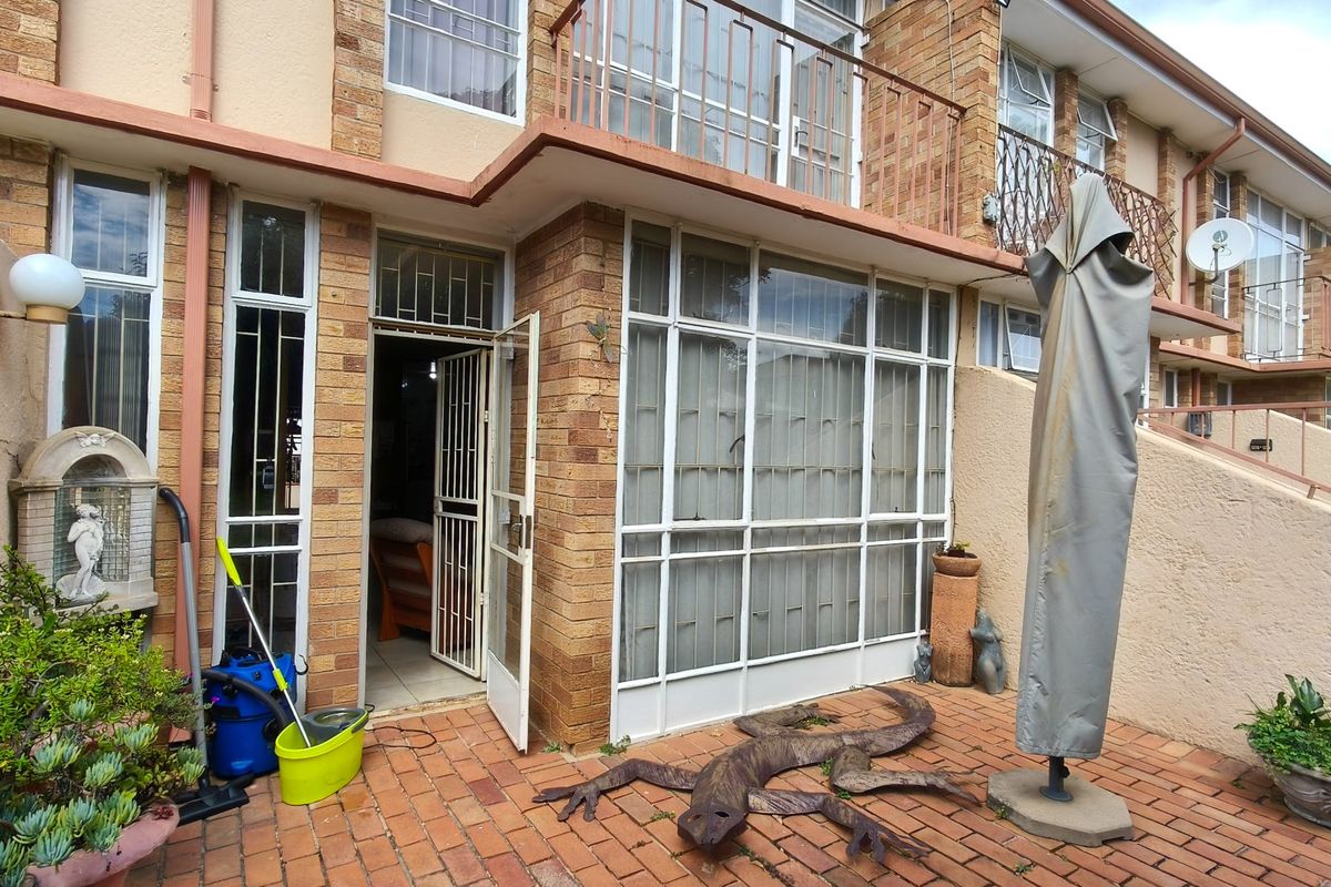 Rear exterior view of a townhouse featuring a brick facade, paved patio area, and metal security fixtures on doors and windows.
