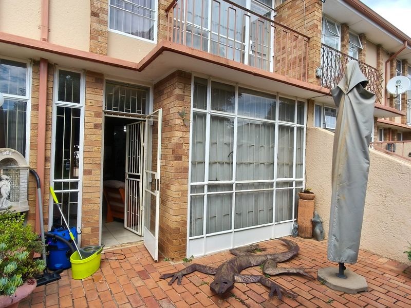 Rear exterior view of a townhouse featuring a brick facade, paved patio area, and metal security fixtures on doors and windows.