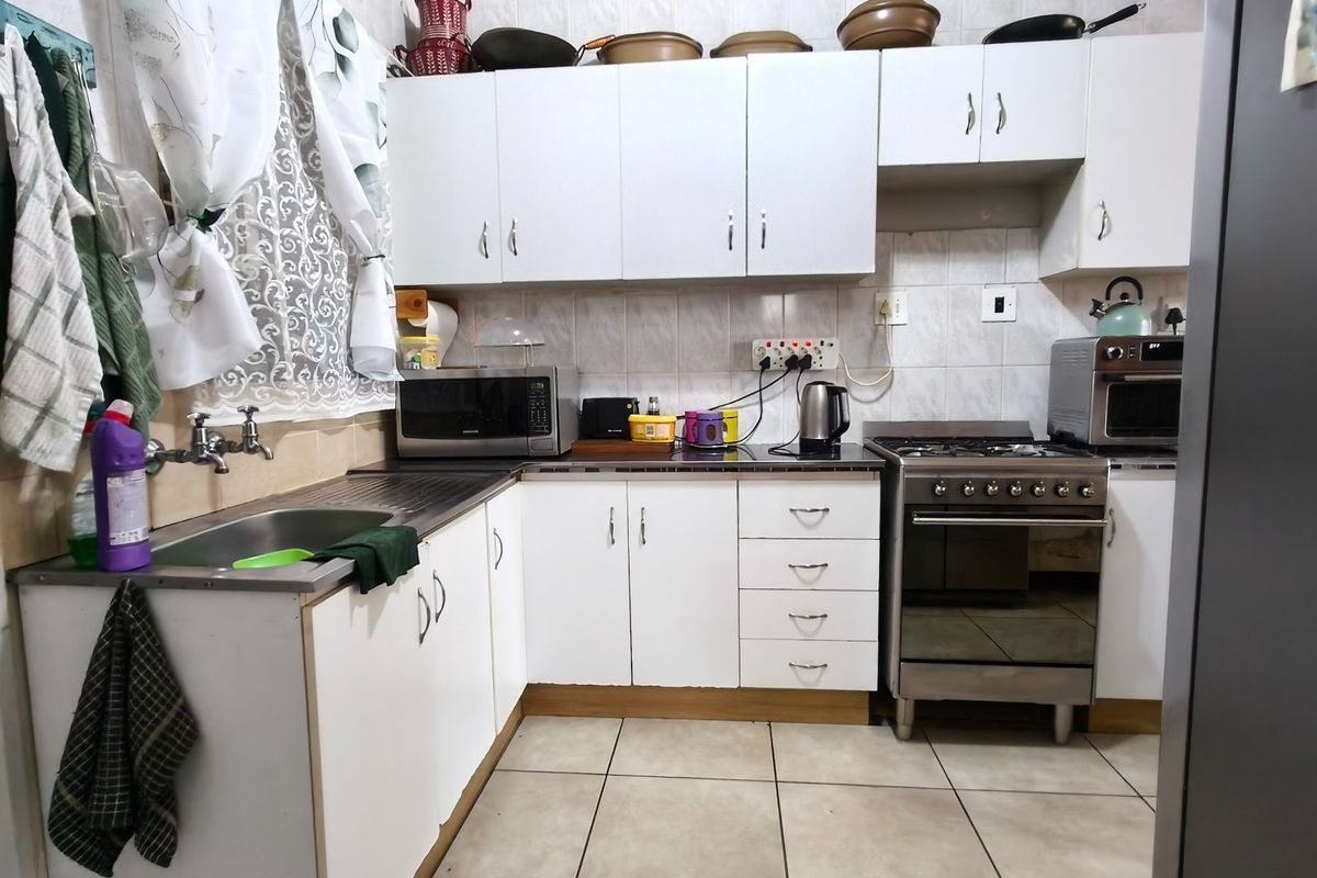 A functional kitchen featuring white cabinetry, tiled backsplash, stainless steel sink, and a gas stove with oven.