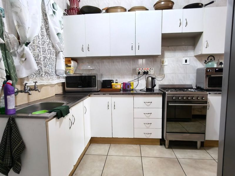A functional kitchen featuring white cabinetry, tiled backsplash, stainless steel sink, and a gas stove with oven.