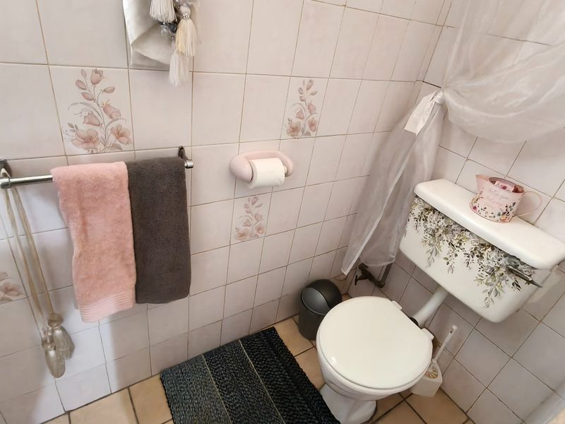A dated bathroom featuring ceramic wall and floor tiles, a standard toilet, and a wall-mounted towel rail.