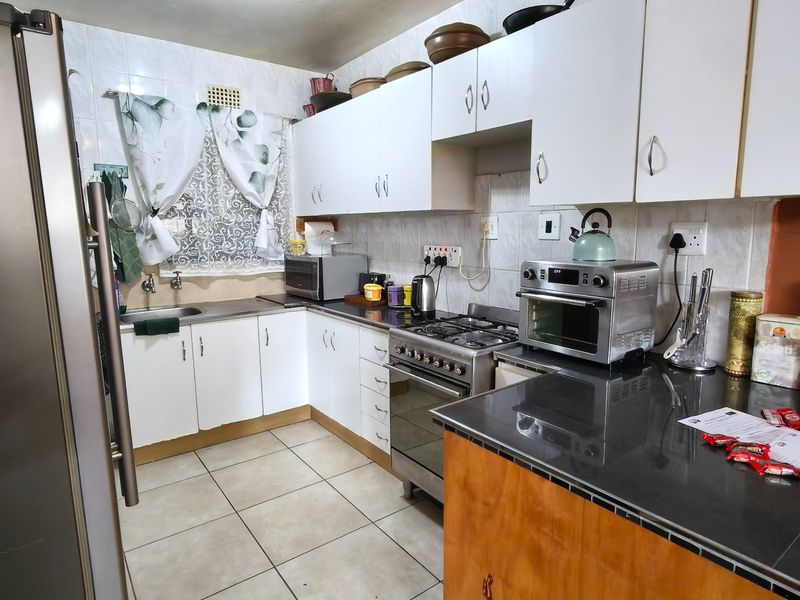 A functional kitchen featuring white cabinetry, tiled backsplash, gas hob, oven, and tiled flooring, offering a practical layout for daily meal preparation.