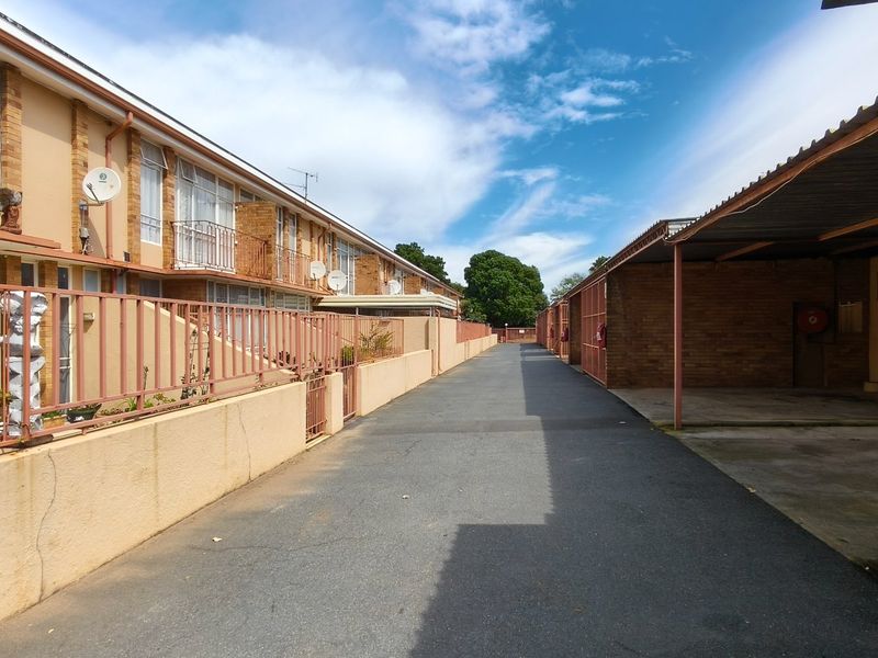 Exterior view of a townhouse complex featuring a paved driveway, covered carport parking, and brick facade buildings with metal balcony railings.