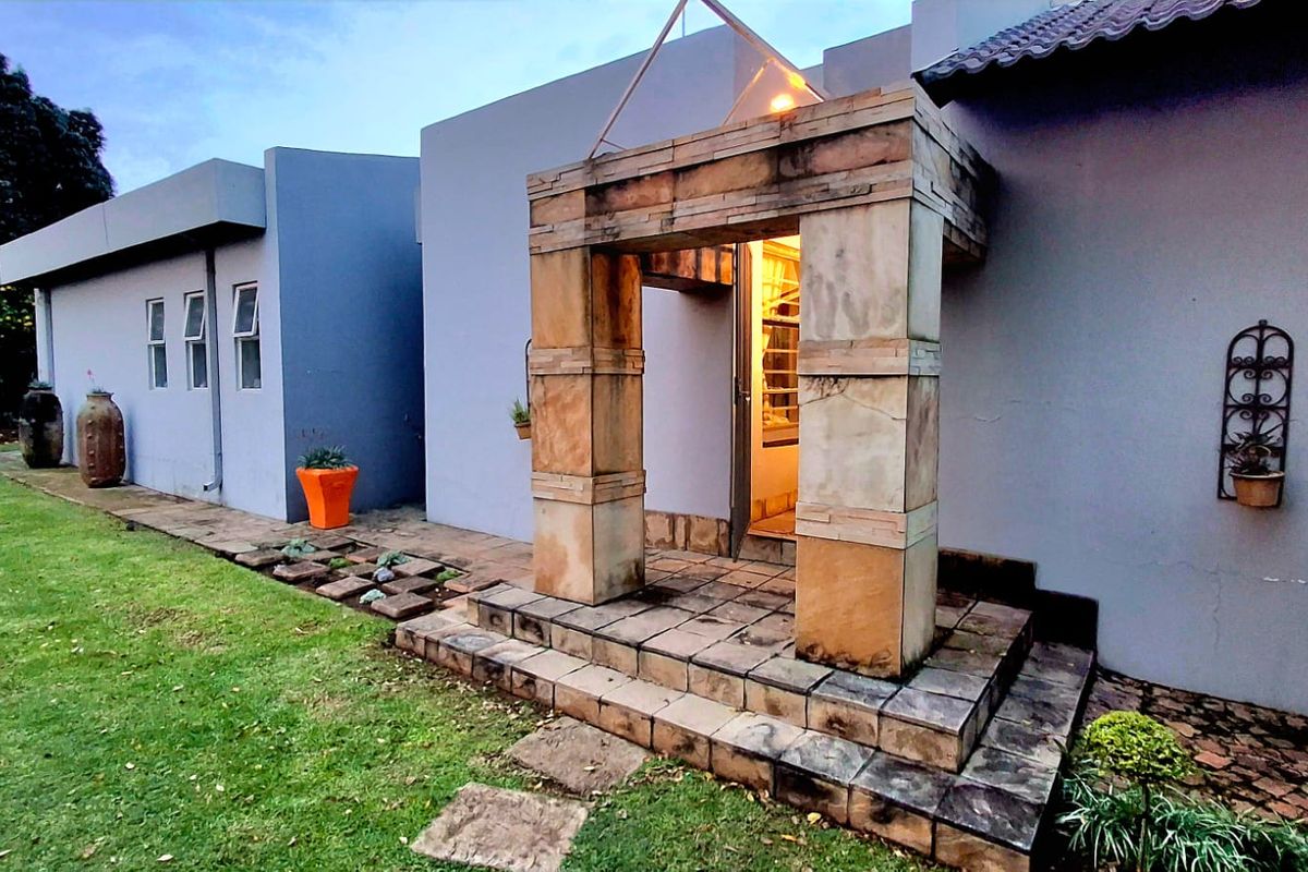 Rear exterior view featuring a stone-clad entrance portico, tiled steps, and a paved patio area adjacent to the garden.