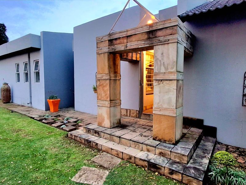 Rear exterior view featuring a stone-clad entrance portico, tiled steps, and a paved patio area adjacent to the garden.