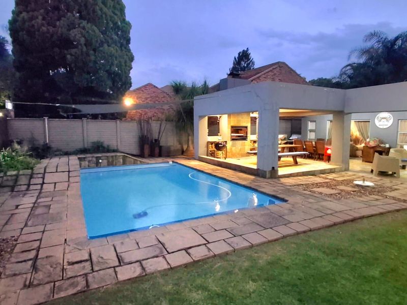Outdoor entertainment area featuring a swimming pool, paved surround, and a covered patio with a built-in braai, perfect for evening relaxation.