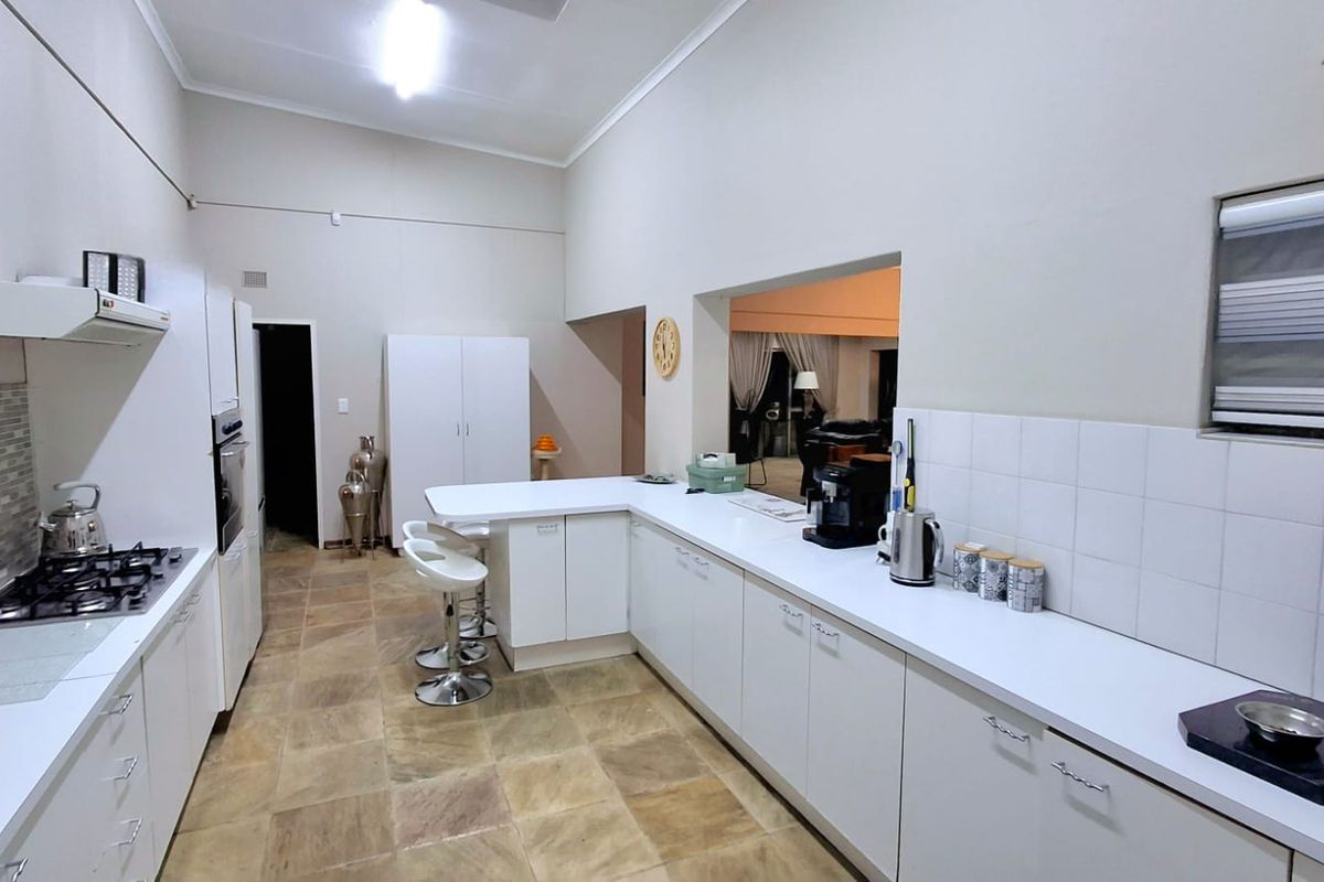 A spacious kitchen featuring white cabinetry, a gas hob with extractor, built-in oven, and a breakfast counter, finished with tiled flooring and backsplash.