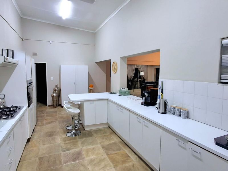 A spacious kitchen featuring white cabinetry, a gas hob with extractor, built-in oven, and a breakfast counter, finished with tiled flooring and backsplash.