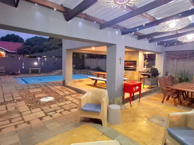 Spacious covered patio area featuring a built-in braai, exposed timber beams, and direct access to a private swimming pool and garden.