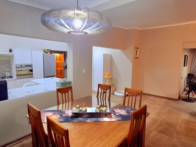 Open plan dining area flowing into a functional kitchen with built-in oven, hob, and breakfast counter, featuring tiled flooring throughout.