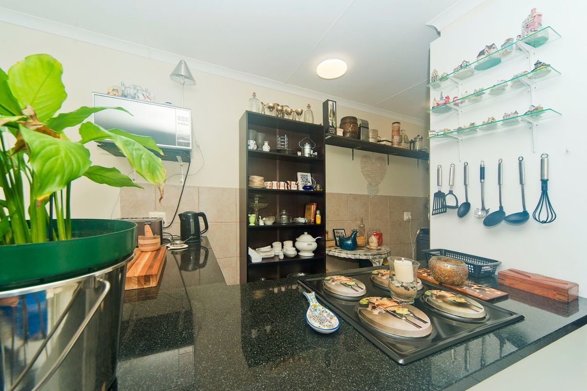 A functional kitchen featuring dark granite countertops, a built-in hob, tiled backsplash, and practical wall-mounted shelving for storage.