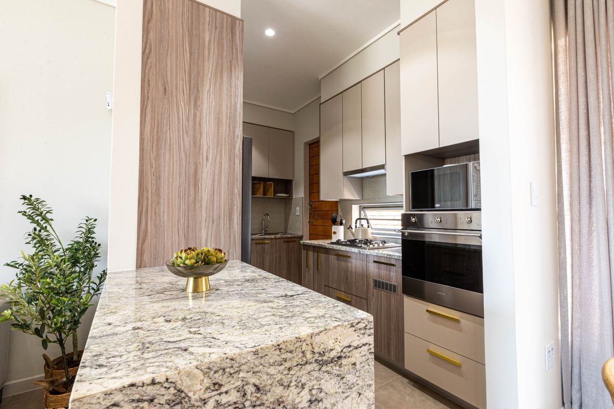 Modern kitchen featuring granite countertops, integrated appliances including an oven and microwave, and sleek wood-finish cabinetry with ample storage space.