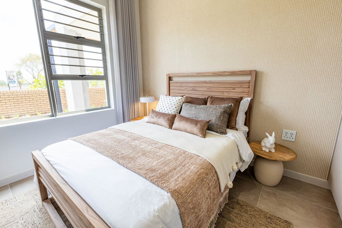 A well-maintained bedroom featuring neutral textured wallpaper, tiled flooring, and a large aluminium-framed window providing natural light.
