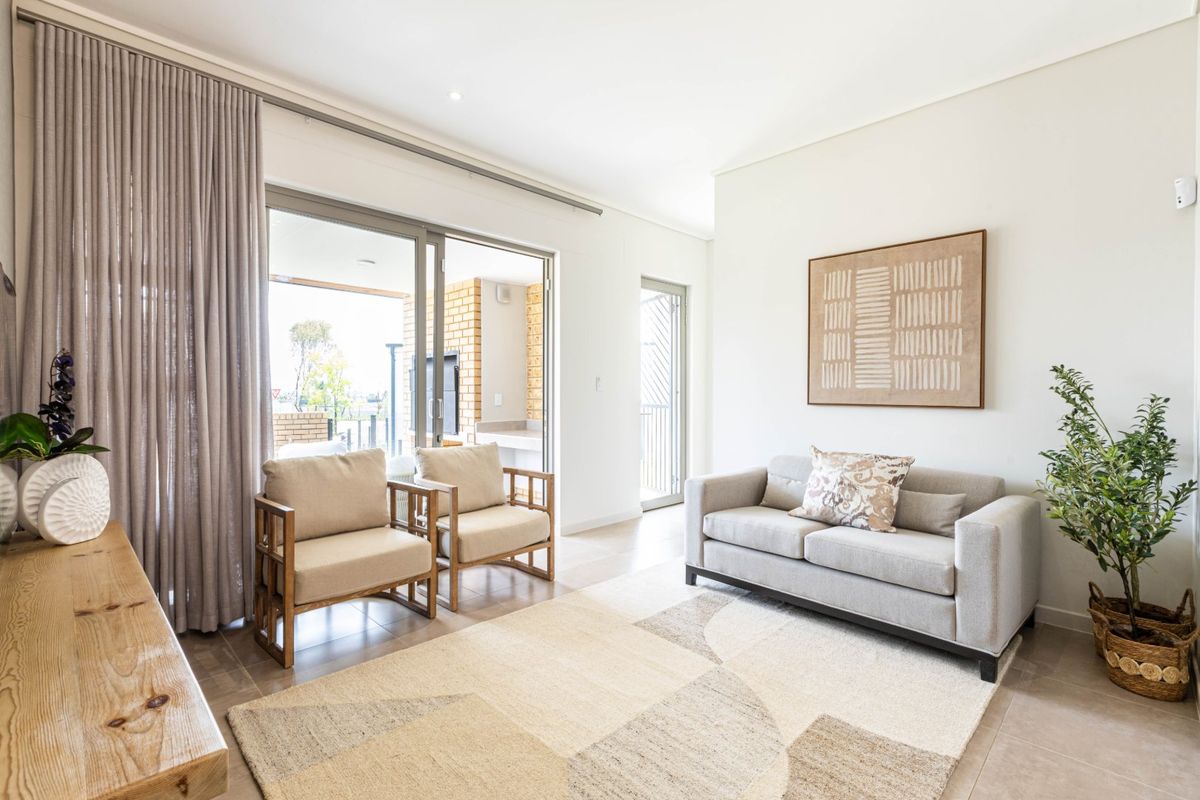 A bright and modern living room featuring neutral tiled floors, recessed lighting, and large sliding glass doors providing seamless access to the outdoor patio area.