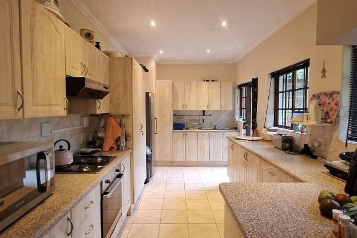 A functional kitchen featuring light wood cabinetry, granite countertops, built-in oven, gas hob, and tiled flooring with ample natural light.
