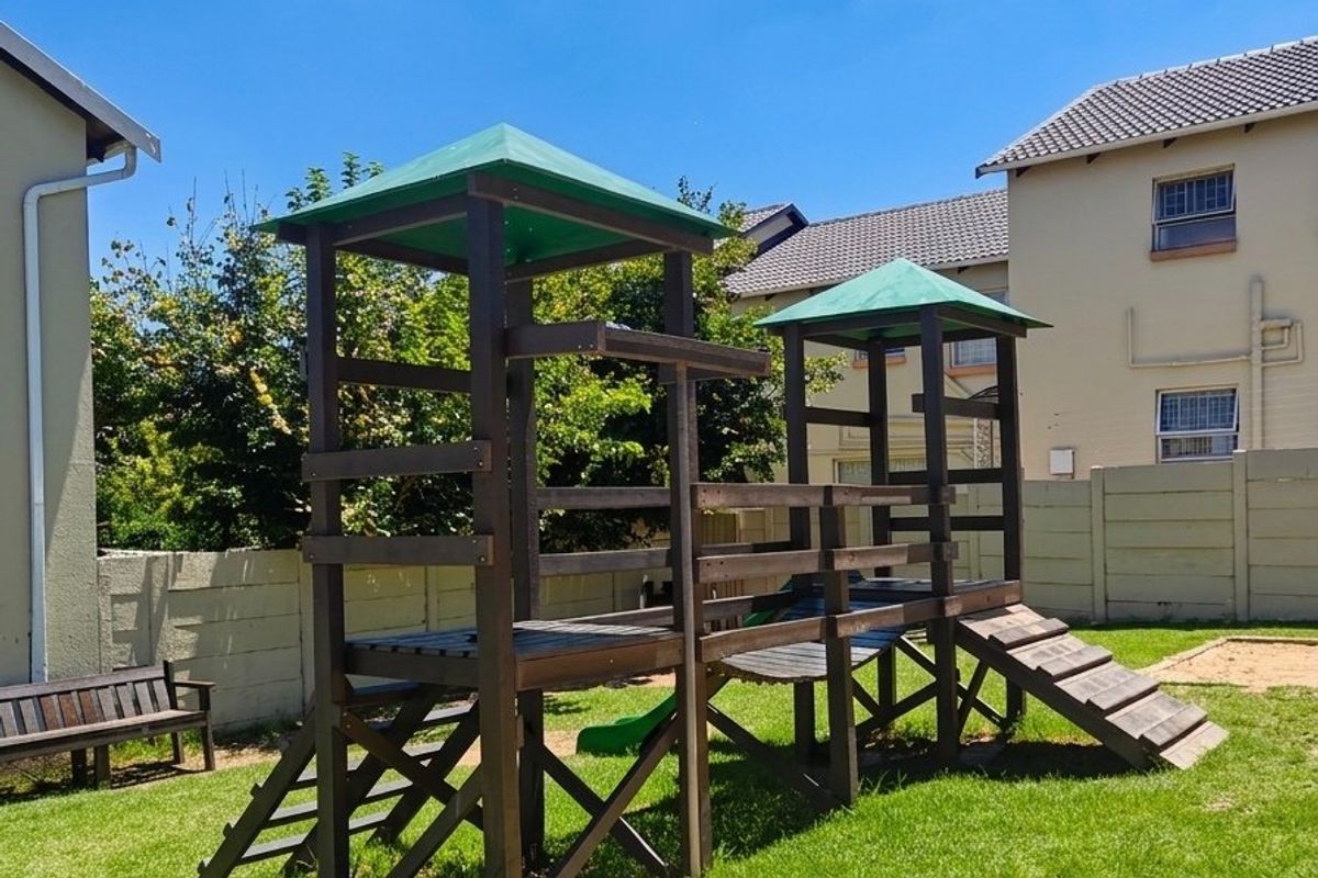A well-maintained rear garden area featuring a wooden jungle gym, a sandpit, and a secure precast concrete boundary wall.