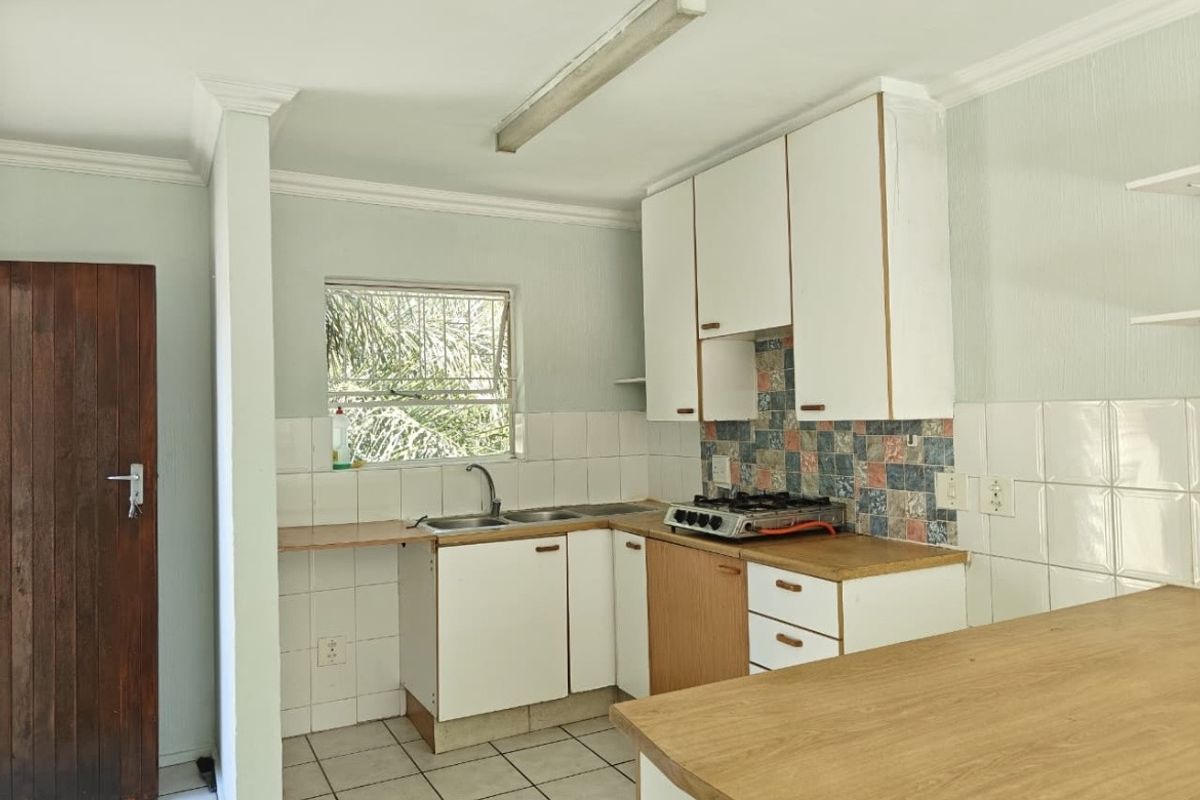 A functional kitchen featuring built-in cabinetry, a double sink, and a gas hob, with tiled splashbacks and flooring throughout.