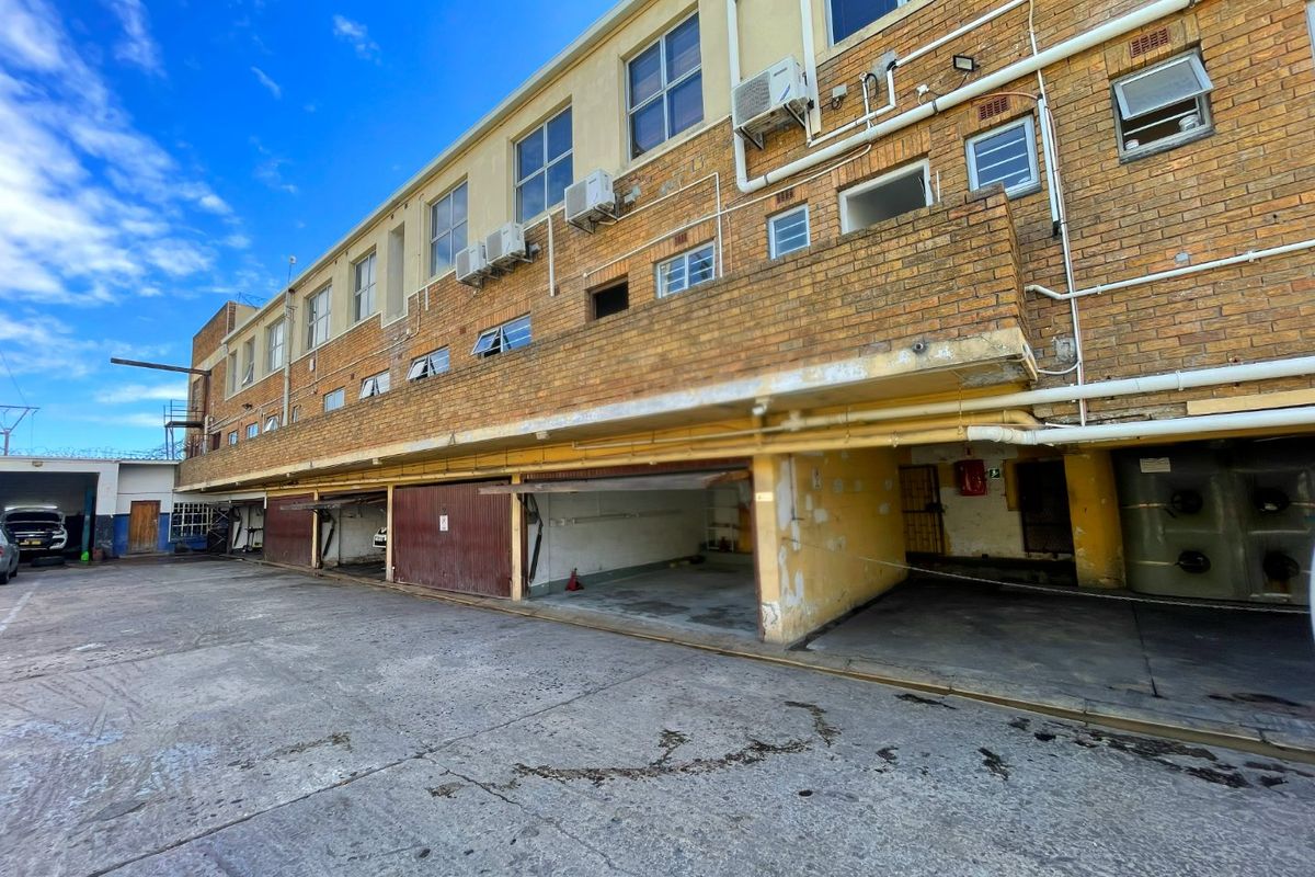 Rear exterior view of a commercial building featuring multiple garage bays, brick facade, and external air conditioning units with paved driveway access.