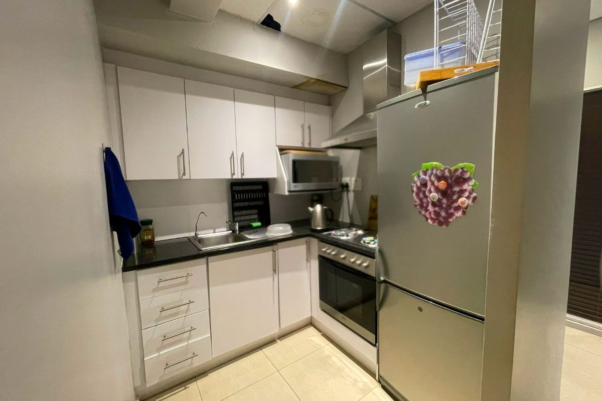 Compact kitchen featuring white cabinetry, black countertops, built-in oven, hob, and extractor fan, with visible ceiling damage requiring repair.