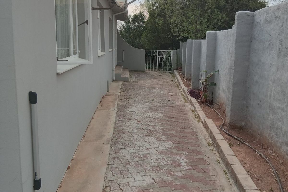A side exterior pathway featuring paved ground, a boundary wall, and a metal gate leading to the rear of the property.