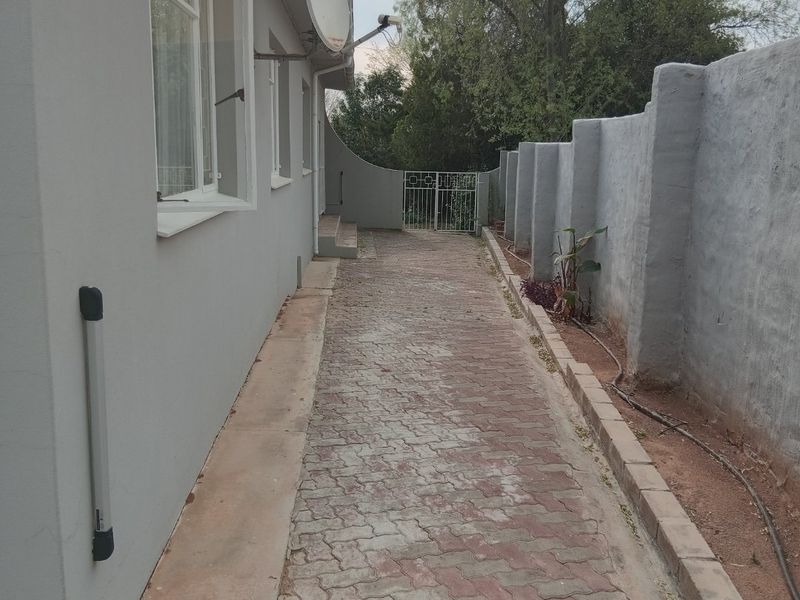 A side exterior pathway featuring paved ground, a boundary wall, and a metal gate leading to the rear of the property.