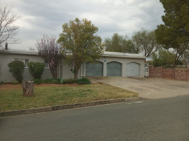 Front view of a single-story house featuring a triple garage with metal roller doors, a concrete driveway, and a brick boundary wall.