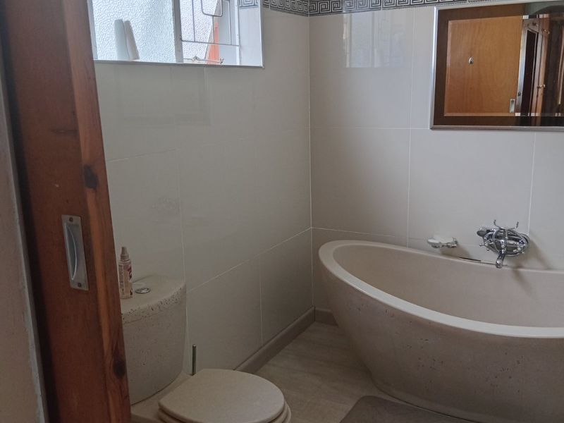 A functional bathroom featuring a freestanding bathtub, toilet, and tiled walls with a decorative border, providing a clean and practical space.
