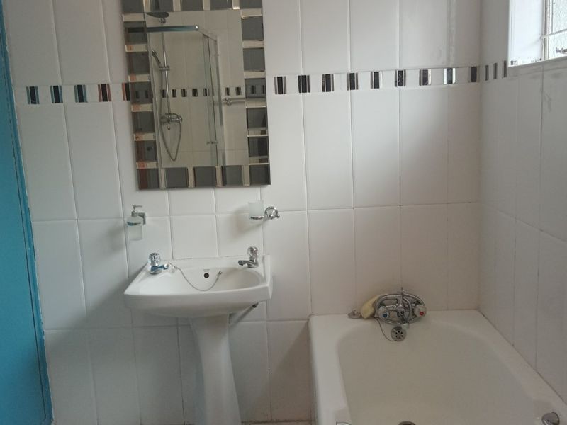 A functional bathroom featuring a pedestal basin, bathtub with chrome fixtures, and white wall tiling with a decorative border.