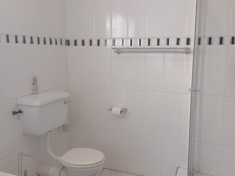 A functional bathroom featuring white wall tiles with a decorative border, a standard toilet, and a glass-enclosed shower area.