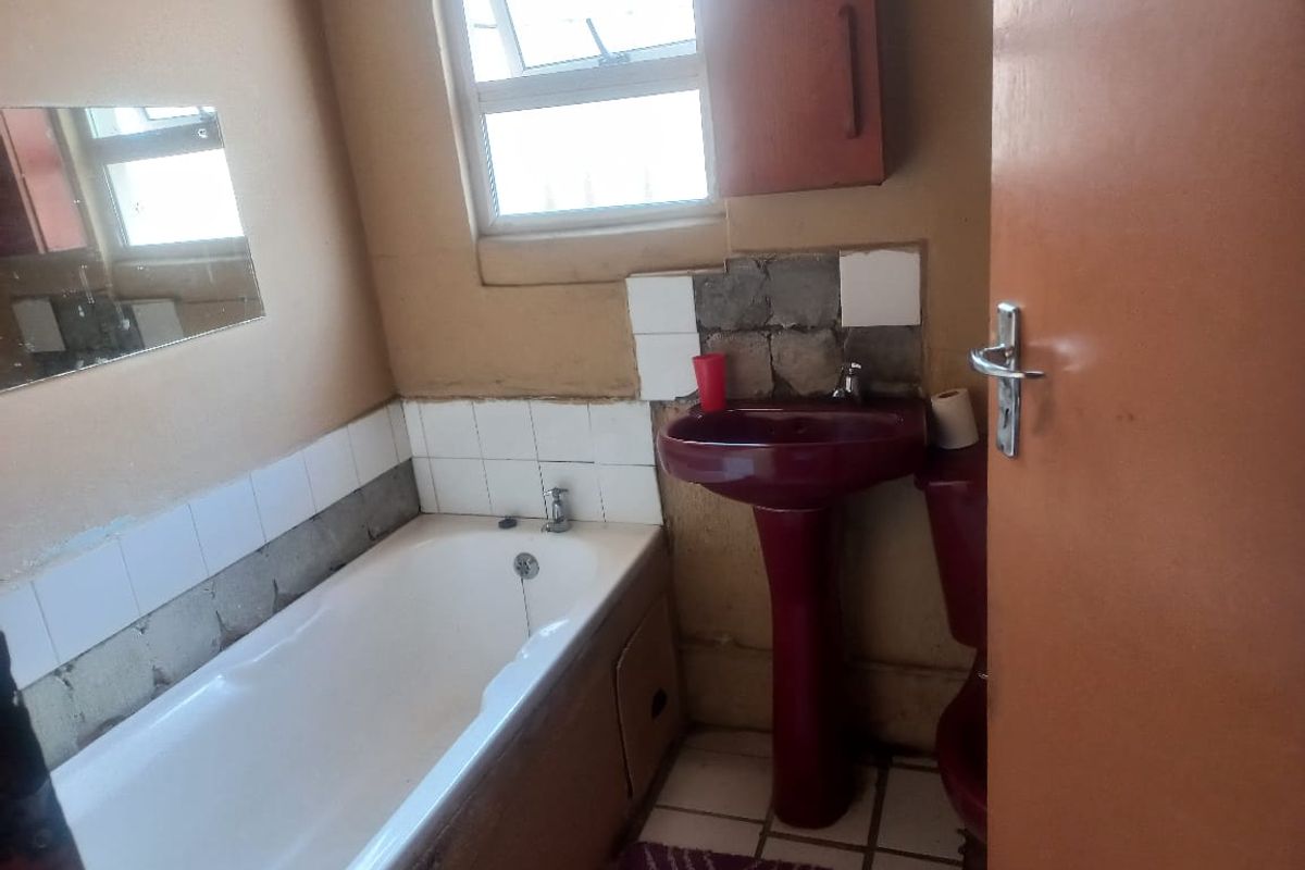 A dated bathroom featuring a white bathtub, a burgundy pedestal basin, and a matching toilet, requiring significant cosmetic updates and tile repairs.
