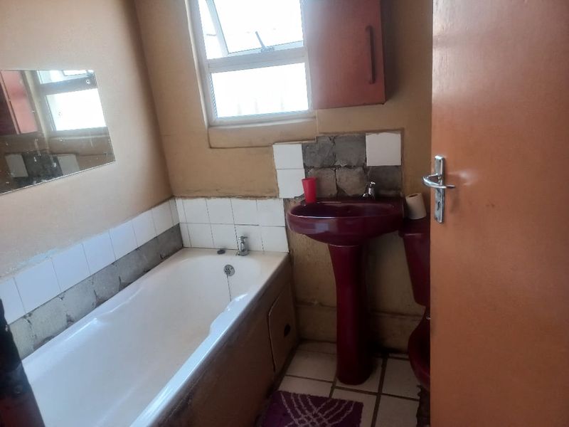 A dated bathroom featuring a white bathtub, a burgundy pedestal basin, and a matching toilet, requiring significant cosmetic updates and tile repairs.